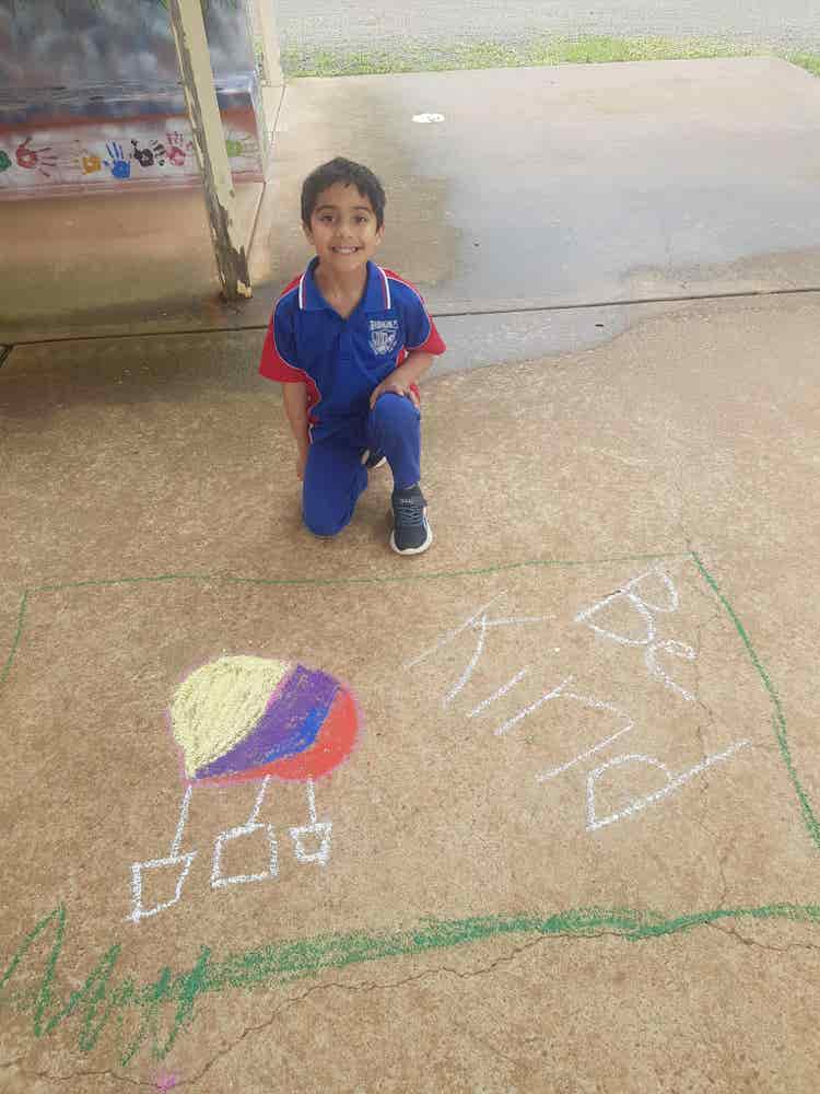 An image of a Kindergarten student with their chalk drawing about kindness.
