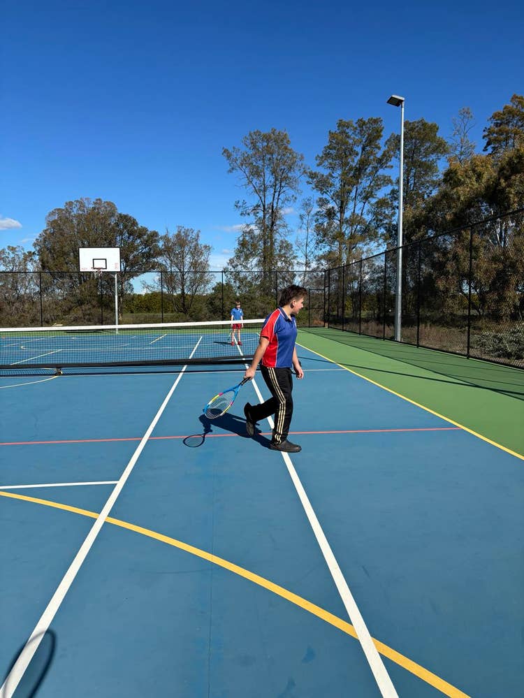 An image of two students using the multi-purpose sports court for tennis skills development.